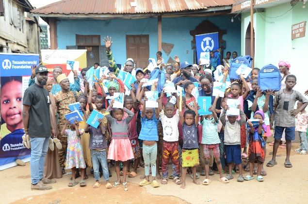 Children in a Nigerian community hold up notebooks and school bags donated by TosaadecWorld Foundation during an outreach visit.